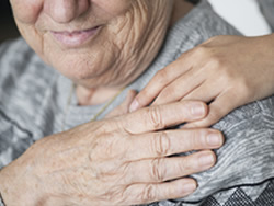 Elderly woman smiling with caretaker's hand on her shoulder. Image courtesy of Rawpixel.com - Freepik.com