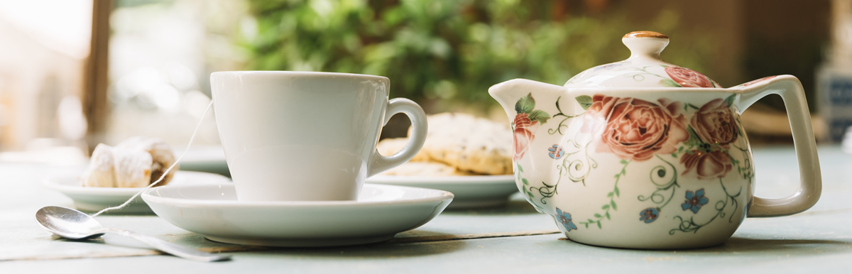 A floral tea pot and tea cup sitting on a table.